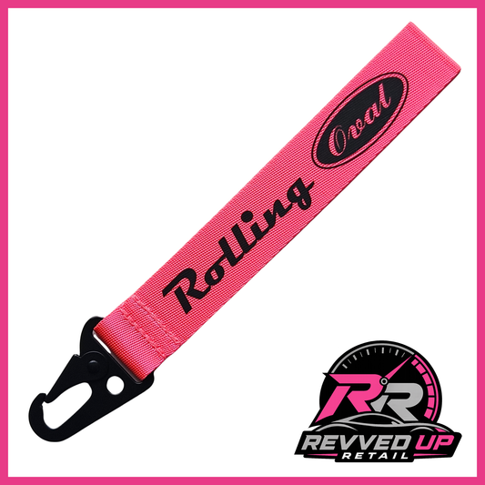 A Rolling Oval brand wristlet strap in fuchsia pink with black printed logos and a black metal carabiner clip, shown on a white background with a Revved Up Retail watermark.