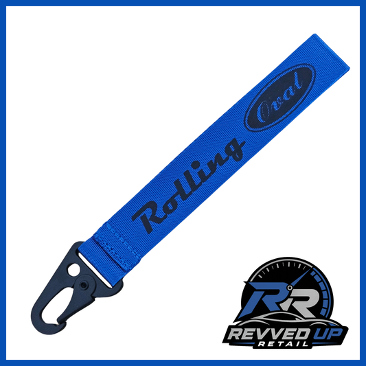 A Rolling Oval brand wristlet strap in blue with black printed logos and a black metal carabiner clip, shown on a white background with a Revved Up Retail watermark.